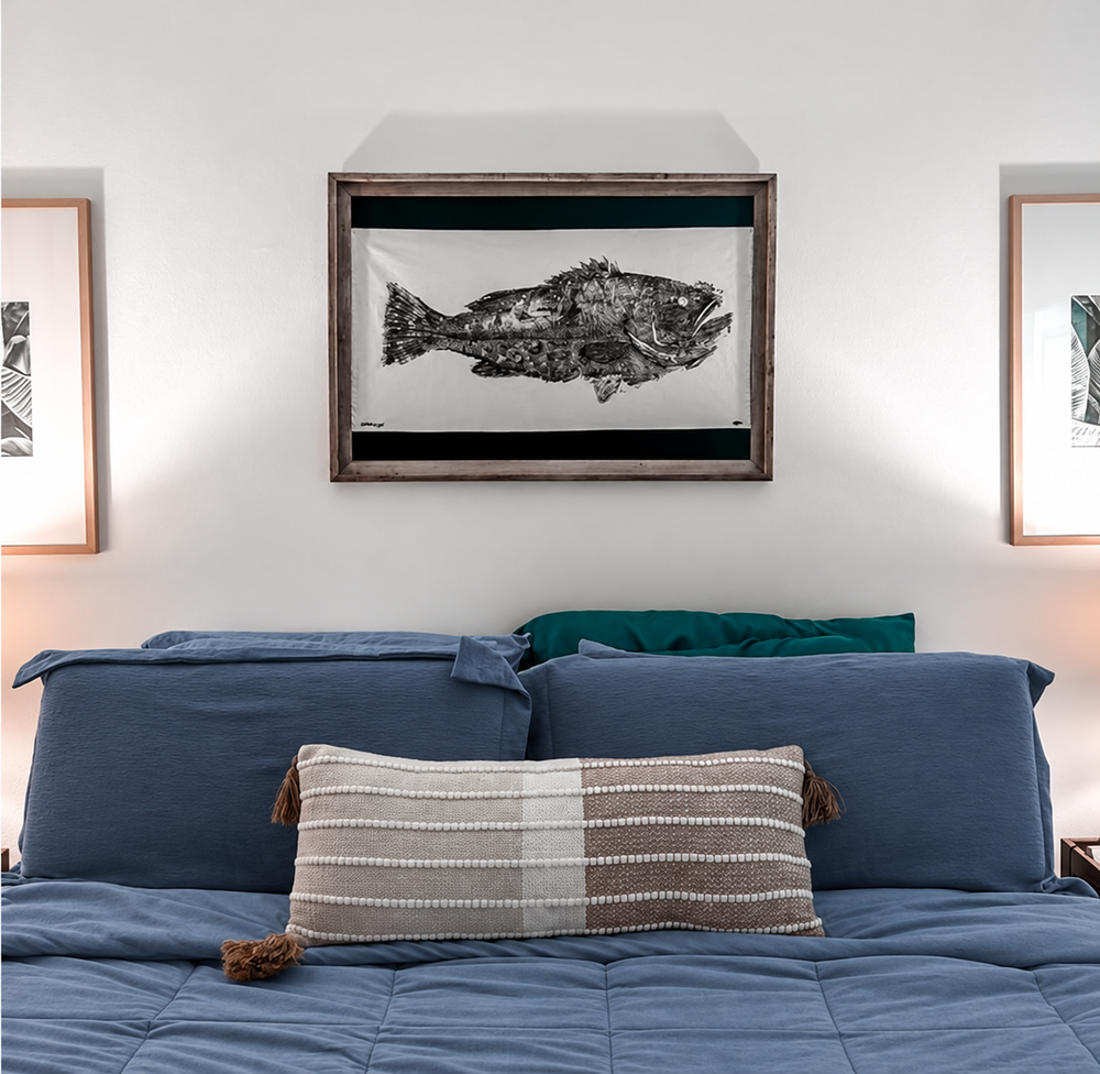 Framed Gyotaku fish print above a bed with blue bedding
